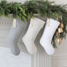 three stockings hanging from a mantel decorated with greenery and gold bells, on top of a mantle