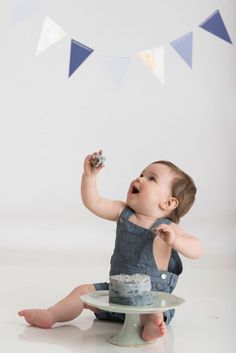 a baby sitting on the floor eating cake with bunting flags in the back ground