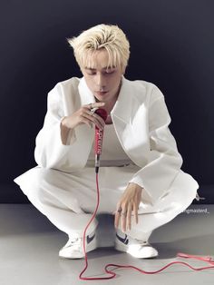 a man sitting on the ground with a microphone in his hand and wearing white clothes