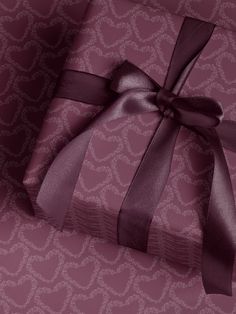 a gift wrapped in purple ribbon with a bow on it's side, sitting against a patterned background