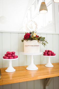 a white cake sitting on top of a wooden table next to red macaroons