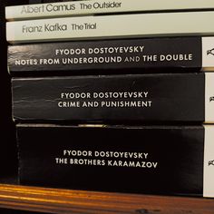 five books stacked on top of each other in front of a wooden book shelf with black and white lettering