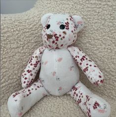 a white teddy bear sitting on top of a couch next to a pillow covered in pink and red flowers