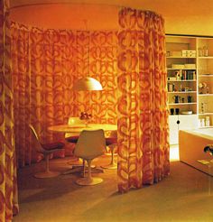 an orange curtained room with a table and chairs in it, next to a book shelf