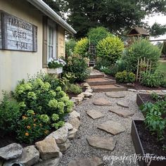 a garden with rocks and plants in front of a small house that has a sign on the side of it