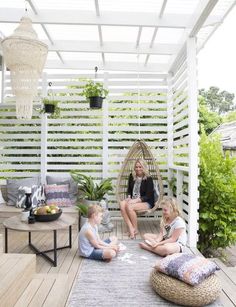 a woman and two children sitting on a porch with a hammock hanging from the ceiling