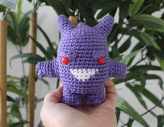 a purple crocheted stuffed animal with red eyes and fangs on it's face