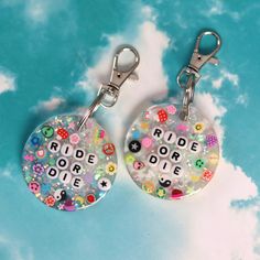 two keychains with the words ride or die printed on them, sitting in front of a cloudy sky