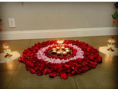 a heart - shaped arrangement of flowers and lit candles on the floor in front of a wall