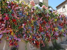 a wall covered in lots of colorful flowers next to a building with a clock on it