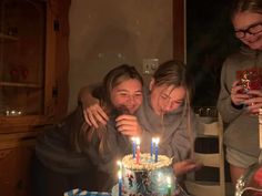 two girls are hugging each other while looking at a birthday cake with candles on it