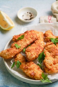 some fried food on a white plate with lemon wedges and seasoning next to it