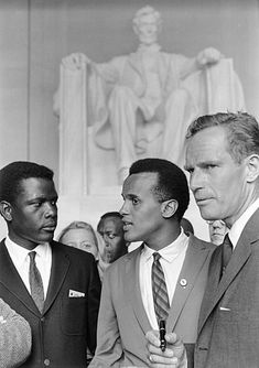 black and white photograph of three men in suits standing next to each other near a statue