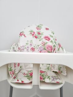 a white high chair with pink and green flowers on it's seat cushiones