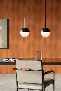 two hanging lights above a table with chairs and plates on it, in front of an orange wall