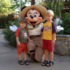 two boys standing next to mickey mouse in front of an animal statue at disney world