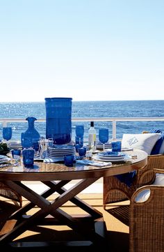 an outdoor table with blue vases and plates on it near the water's edge