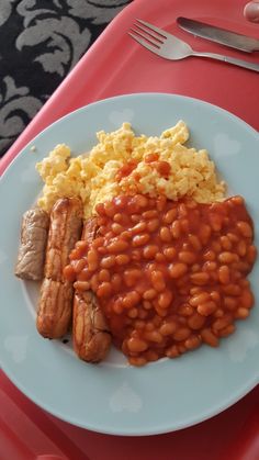 a white plate topped with beans and sausage next to scrambled eggs on a red tray