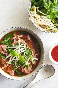 a bowl of soup with meat and vegetables next to a small bowl of ketchup