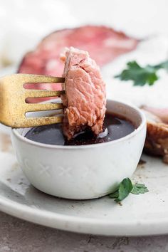 a piece of meat is being lifted out of a bowl with sauce and a fork