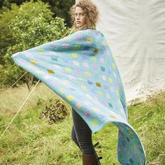 a woman standing in the grass holding a blue and yellow blanket over her head with polka dots on it