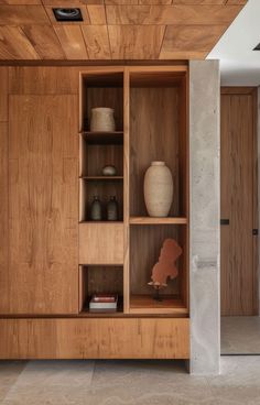 an open wooden cabinet with vases and books on it's shelves in the living room