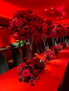 a long table with red flowers in vases on it and chairs around the table