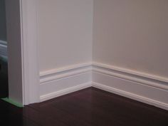 an empty room with hard wood flooring and white walls, along with a black cat