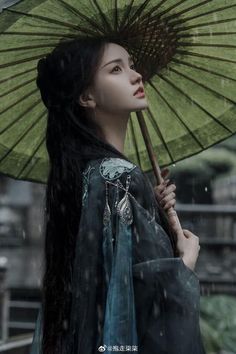 a woman with long black hair holding an umbrella in the rain, looking up at something