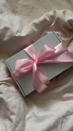 an open box with pink ribbon laying on a bed