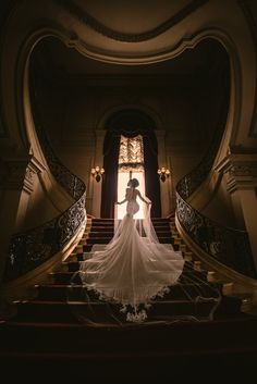 a woman in a wedding dress is standing on some stairs with her arms behind her back