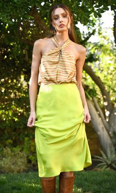 a woman standing in the grass wearing a yellow skirt and brown knee high heel boots