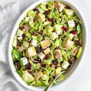 a white bowl filled with shaved brussels sprouts and cranberry bits next to a spoon