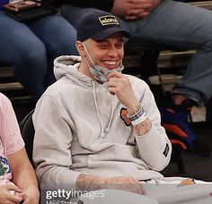 two people sitting next to each other at a basketball game, one wearing a hat and the other smiling