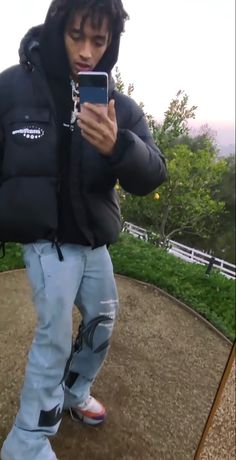 a man standing on top of a hill looking at his cell phone while wearing a black jacket