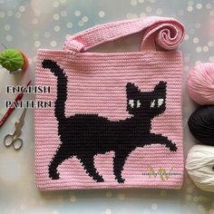 a crocheted bag with a black cat on it and yarn next to it