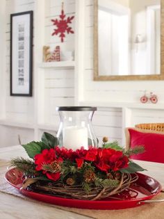 a candle sits on top of a red plate with holly and poinsettis