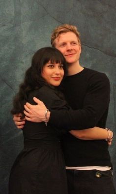 two people hugging each other in front of a wall