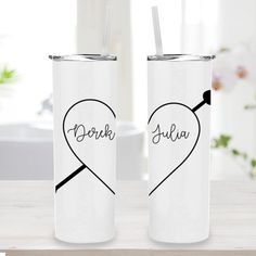 two white tumblers with black writing on them, one has a heart and the other has an arrow