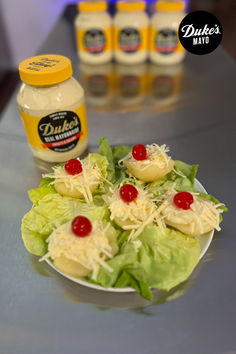 lettuce with cheese and cherries on a plate next to jars of mayonnaise