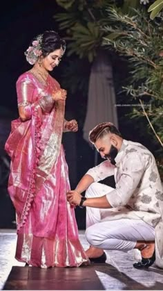 a man kneeling down next to a woman in a pink sari and white dress