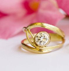 two gold rings with a diamond in the middle and pink flowers behind them on a white surface