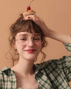 a woman wearing glasses and holding a cupcake on her head, with one hand over her head