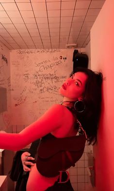 a woman standing in a bathroom next to a wall with writing on it and holding her hand out