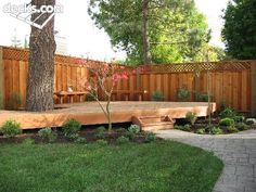 a wooden deck in the middle of a yard next to a tree and some grass