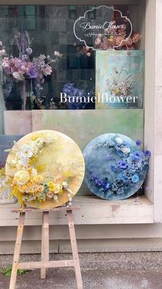 two paintings on easels in front of a flower shop