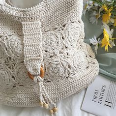 a white crocheted bag sitting on top of a bed next to a bouquet of flowers