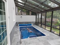 an indoor swimming pool with glass walls and doors on both sides, in the middle of a backyard