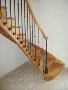 a wooden staircase with black railing and handrails on tiled floor next to white wall