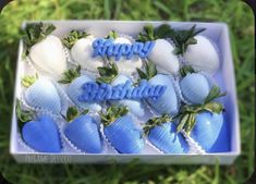 blue and white strawberries in a box with happy birthday written on them, surrounded by greenery